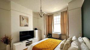 Ein Schlafzimmer mit einem Bett, einem Fernseher, einem Schreibtisch und einem Sessel.