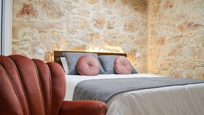A bedroom with a stone wall, a bed with grey and pink pillows, and a brown armchair.