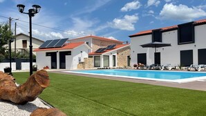 A modern outdoor pool area with a clear blue sky, a well-maintained lawn, and a stone wall.