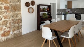 A modern kitchen with white cabinets, a wooden dining table, and a stone accent wall.