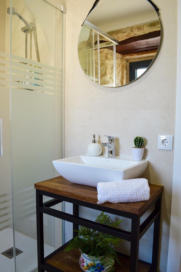 A bathroom with a white sink, a round mirror, a shower, and a small potted plant.