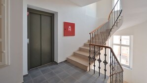 A staircase with a handrail, a red emergency exit sign, and a door with a window.
