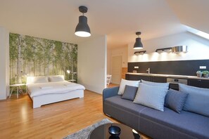 A modern bedroom with a bed, a sofa, and a dining area with a kitchen in the background. - Cozy Riverside Escape. Pet friendly! (Hlavní město Praha)