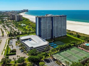 A high-rise hotel with a beach view, a tennis court, and a parking area. - 2BR, 2BA beachfront condo in Marco Island with pool, wifi, and full kitchen. (Marco Island)