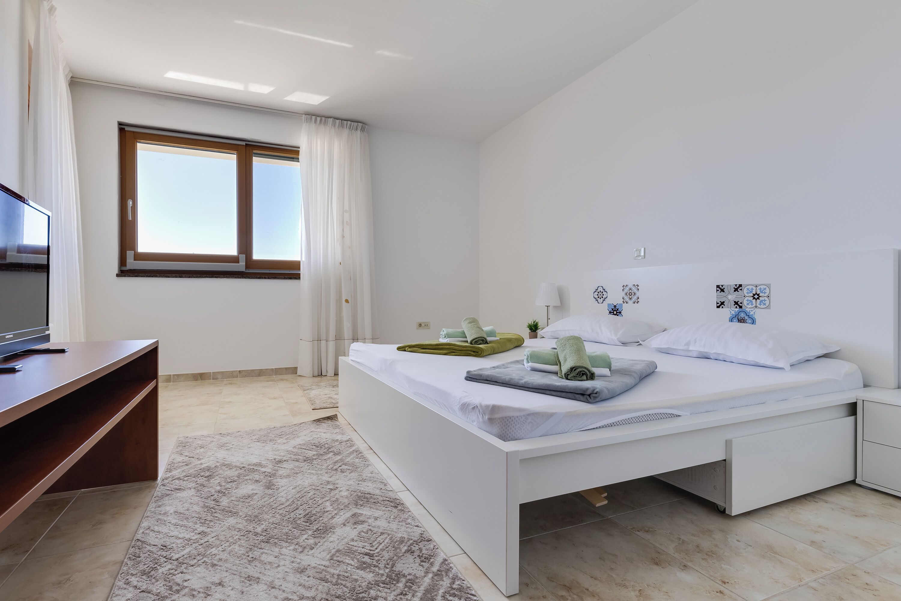 A modern bedroom with a large bed, a TV, and a window with curtains.