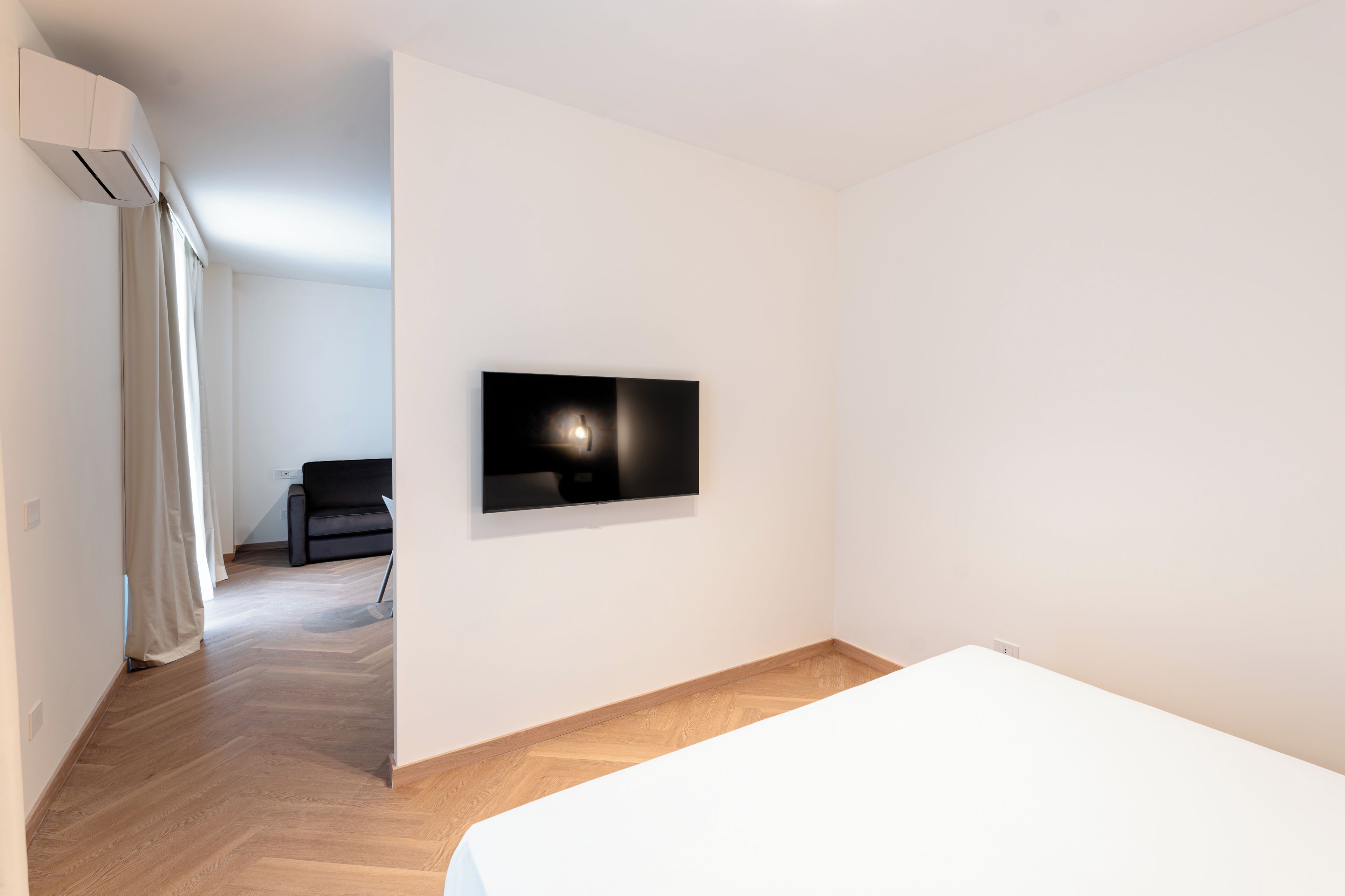 Una habitación de hotel moderna con una cama grande, un televisor montado y piso de madera.