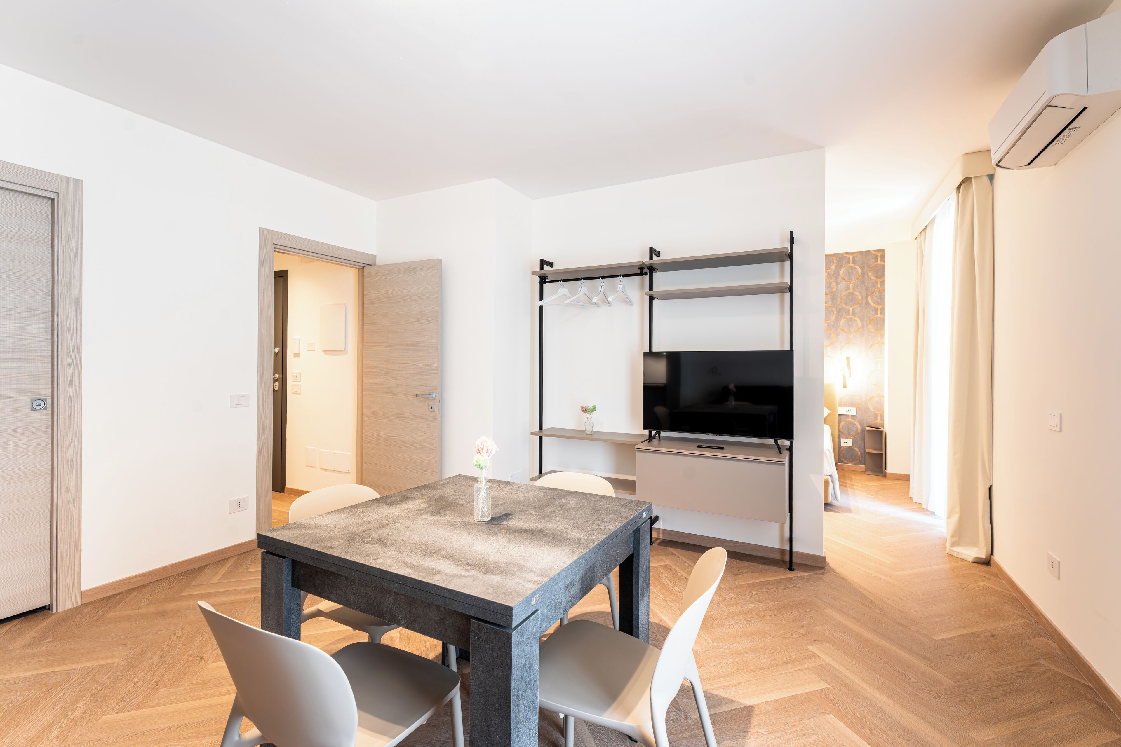A modern kitchen with a large island, a dining area with a table and chairs, and a hallway leading to a bedroom.