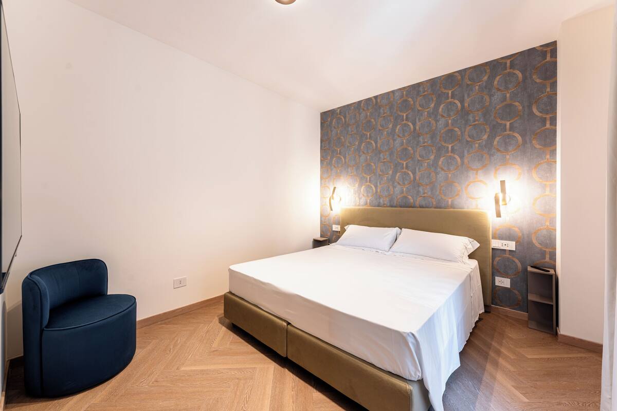 Un dormitorio con cama, mesita de noche, silla y pared con diseño.