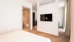A modern hotel room with a large bed, a flat-screen TV mounted on the wall, and a wooden herringbone floor. -  Palazzo Le Giare Luxury Apartments (Bari)