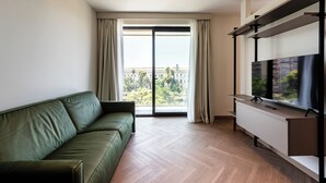 A modern living room with a green sofa, a flat-screen TV on a white cabinet, and a large window with curtains. -  Palazzo Le Giare Luxury Apartments (Bari)