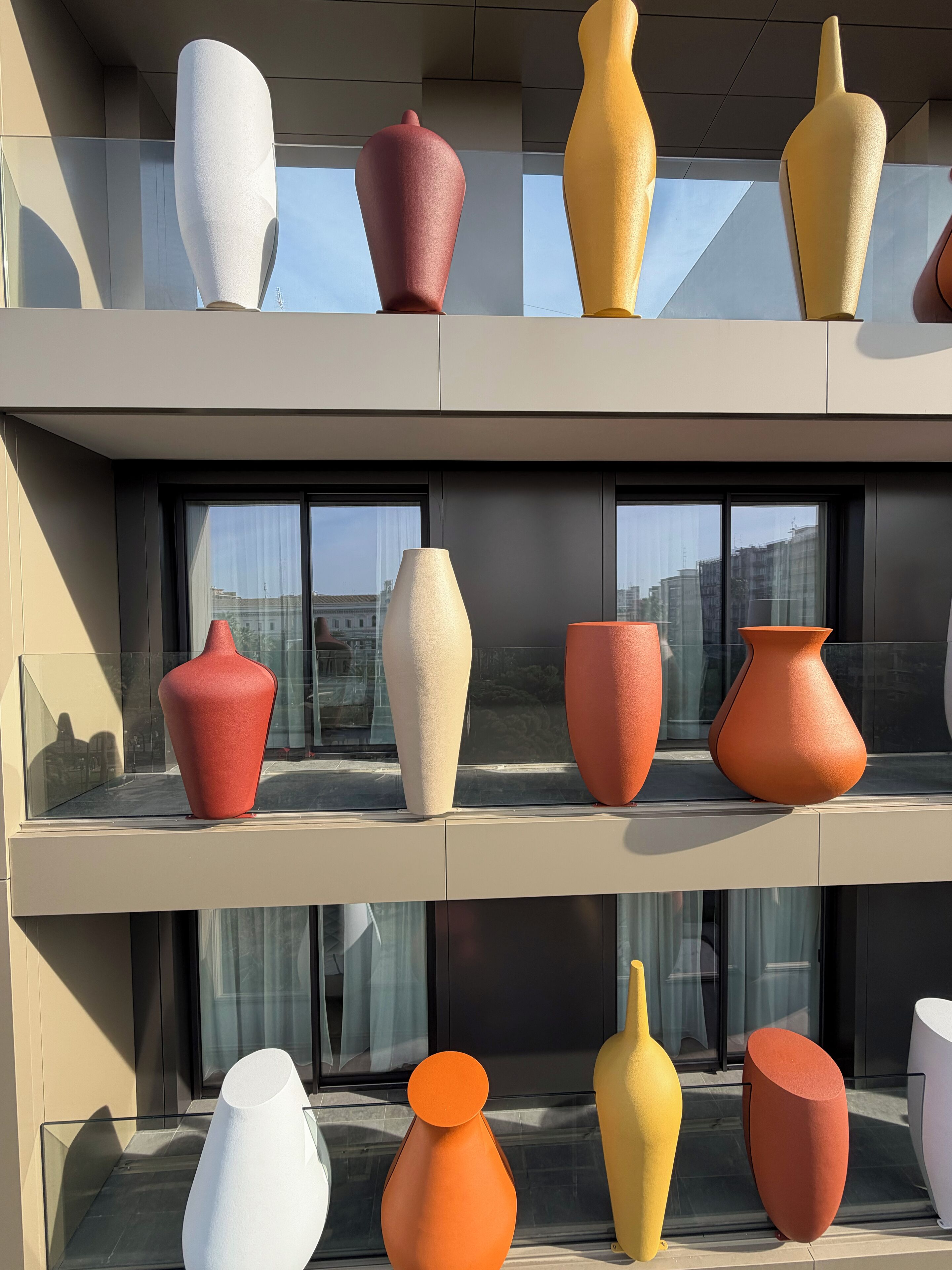 A modern building with multiple floors, each featuring large, uniquely shaped vases displayed in glass cases.