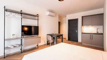 A modern hotel room with a bed, a TV, a desk, and a kitchenette.