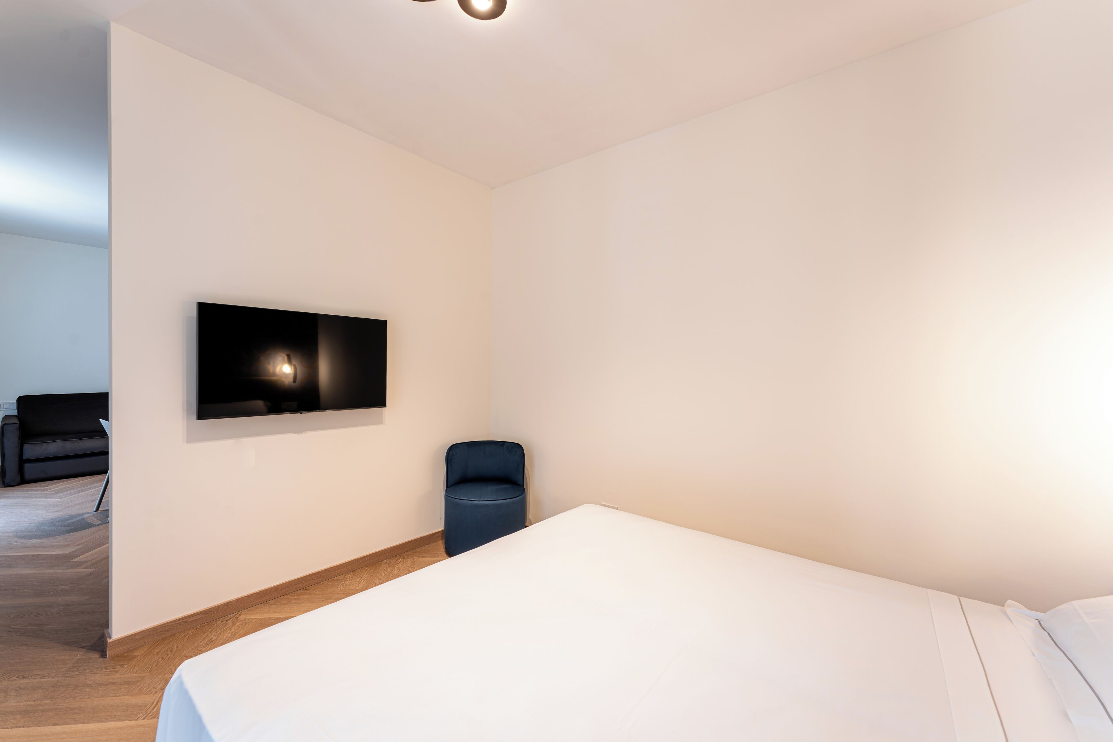A modern hotel room with a large bed, a small seating area, and a flat-screen TV mounted on the wall.