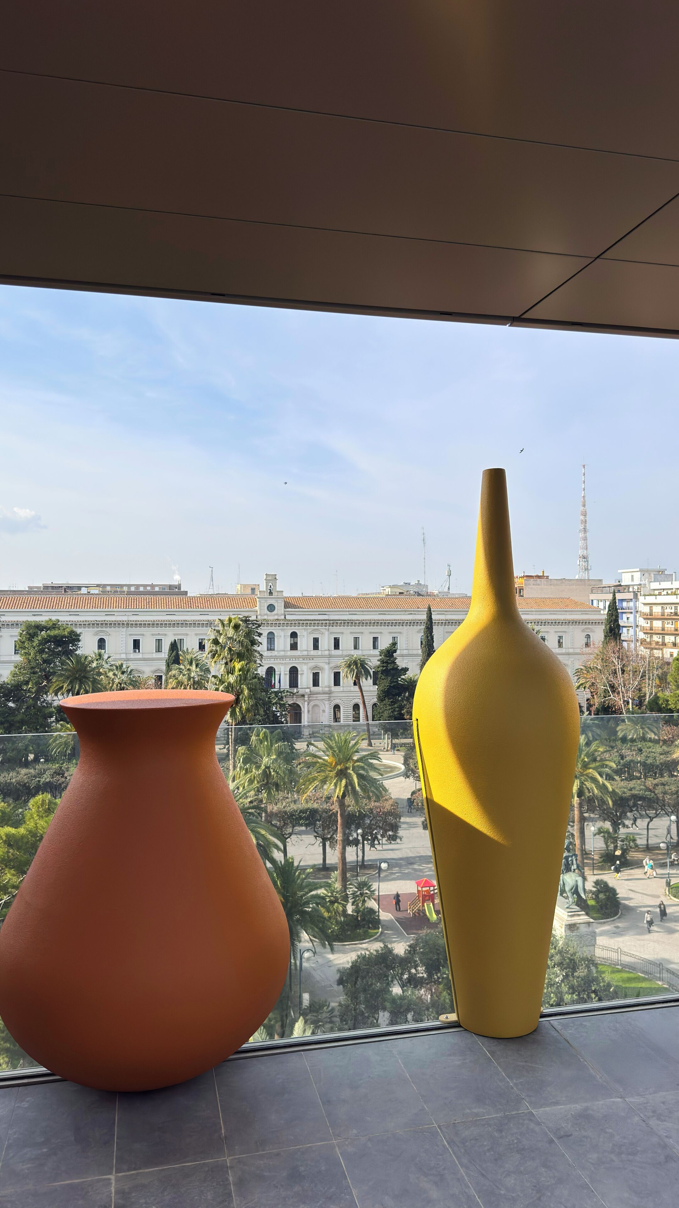 A view from a window with two large vases on a balcony, overlooking a cityscape with historical buildings and a clear sky.