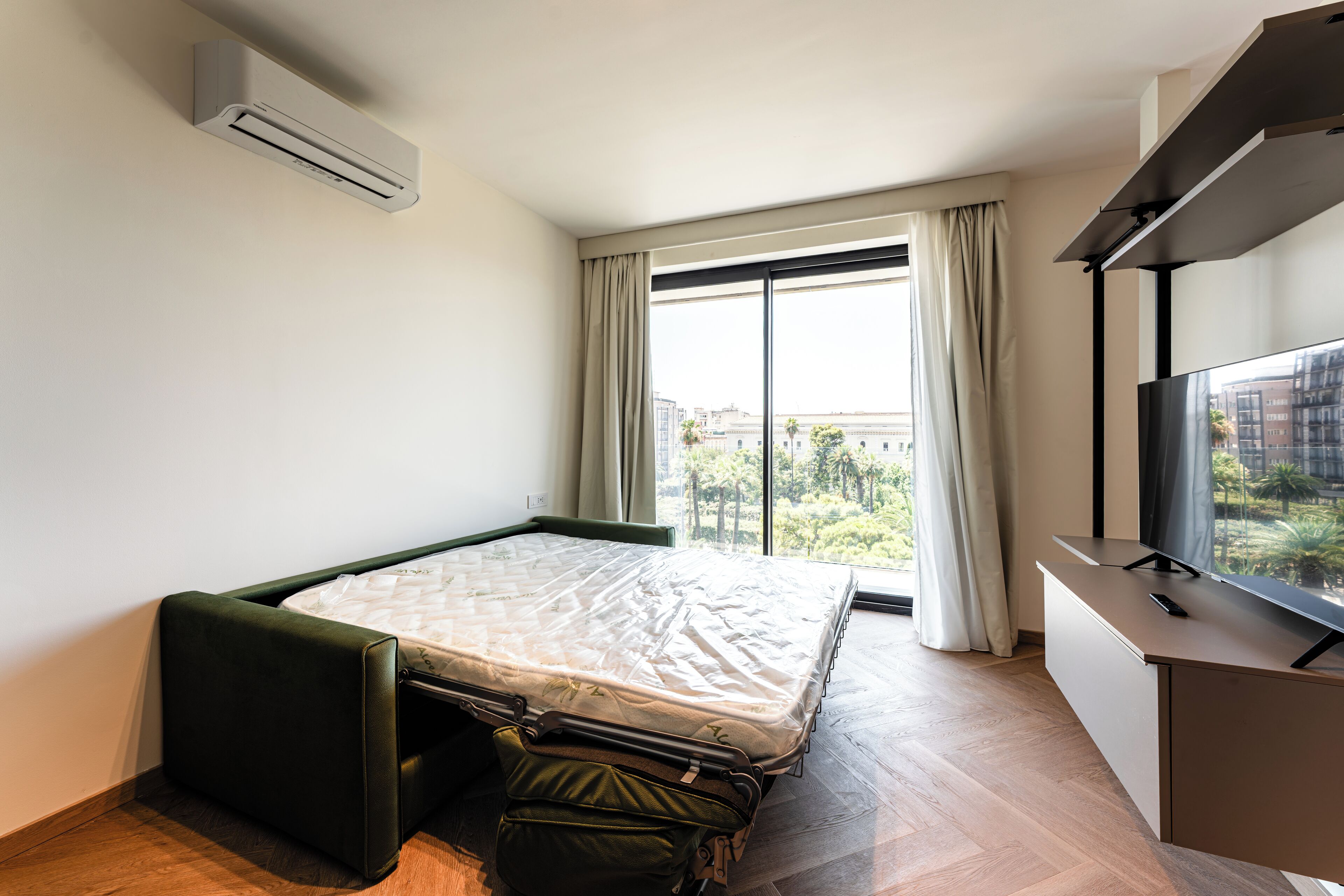 Una stanza piccola con un letto, una scrivania e un'ampia finestra vista città.