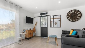 A modern living room with a grey sofa, a large wall clock, and a TV mounted on the wall.