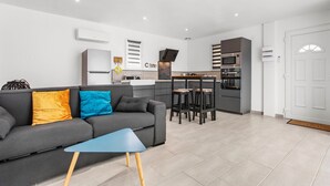 A modern living room with a grey sofa, a blue coffee table, and a kitchen area in the background.