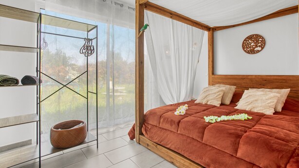 A bedroom with a bed, a window with sheer curtains, a wooden headboard, and a wall decoration.