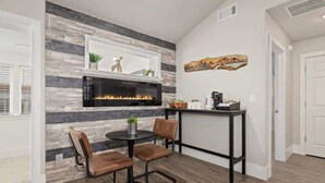 A modern living room with a fireplace, a dining area with two chairs and a table, and a coffee station. - Quiet Razorback Escape - Easy Drive to Downtown & Stadium (Fayetteville)