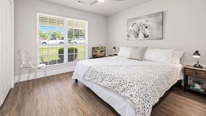 A bedroom with a bed, a ceiling fan, a window with blinds, a chair, and a painting on the wall. - Quiet Razorback Escape - Easy Drive to Downtown & Stadium (Fayetteville)
