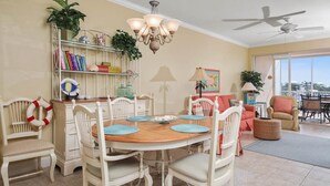 A dining area with a wooden table, white chairs, a chandelier, and a ceiling fan.