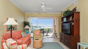 A living room with a sofa, armchair, TV stand, and a balcony with a view.