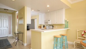 A compact kitchen with white cabinets, a central island with stools, a microwave, and a coffee maker.