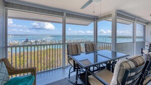 A balcony with a glass table and chairs, overlooking a marina and a bridge. - Boca Grande North - 08: 2BR condo with water views, pool, and hot tub in Boca Grande, FL. (Boca Grande)
