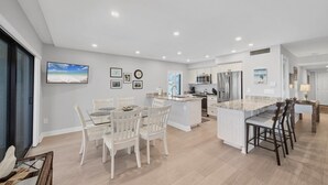 A modern kitchen with white cabinetry, a central island, and a dining area with white chairs. - Charming 2 Bedroom Sea Oats - 237 in Boca Grande, perfect for a relaxing getaway. (Boca Grande)