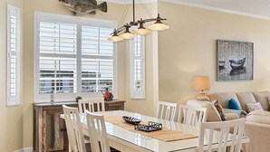 A dining area with a glass table, white chairs, a wooden cabinet, and a view of the sea through large windows. - Boca Vista Harbor - 401D: Spacious 3BR condo in Placida, FL, perfect for 6 guests. (Placida)