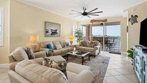A living room with a sofa set, coffee table, and a TV. There is a ceiling fan, a painting, and a view through the glass door to the outside. - Boca Vista Harbor - 401D: Spacious 3BR condo in Placida, FL, perfect for 6 guests. (Placida)