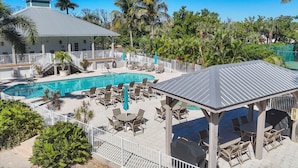 A pool area with lounge chairs and a covered seating area, surrounded by palm trees and a building with a grey roof. - Boca Vista Harbor - 401D: Spacious 3BR condo in Placida, FL, perfect for 6 guests. (Placida)