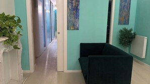 Käytävä, jossa on tummanvihreä sohva, turkoosinsiniset seinät ja huonekasvi.