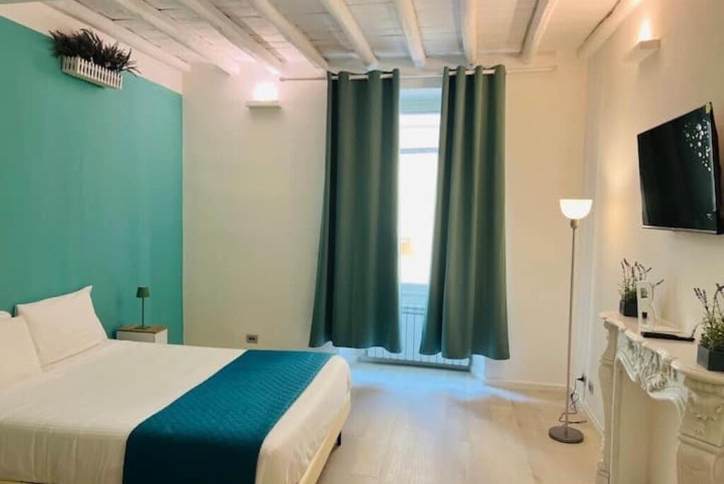 Et hotelværelse med en seng, et natbord, en lampe, et fjernsyn og et vindue med gardiner.