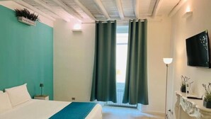 Hotellihuone, jossa on sänky, yöpöytä, lamppu, televisio ja ikkuna, jossa on verhot.