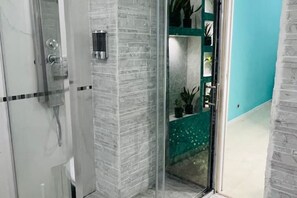 A bathroom with a glass shower enclosure, a marble-tiled wall, and a green shelf with potted plants. - Magic of the Spanish Steps (Roma)