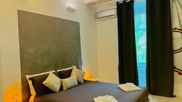 Ein Schlafzimmer mit einem großen Bett, dunklen Vorhängen, einem Fenster und einer Wand-Klimaanlage.
