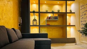 Ein modernes Wohnzimmer mit einem Ecksofa, einer eingebauten Bücherwand mit Pflanzen und einer dekorativen Laterne.