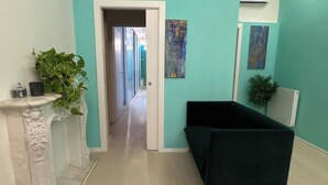 Ein Korridor mit einem dunkelgrünen Sofa, einem weißen Marmor-Kamin und einer Pflanze.