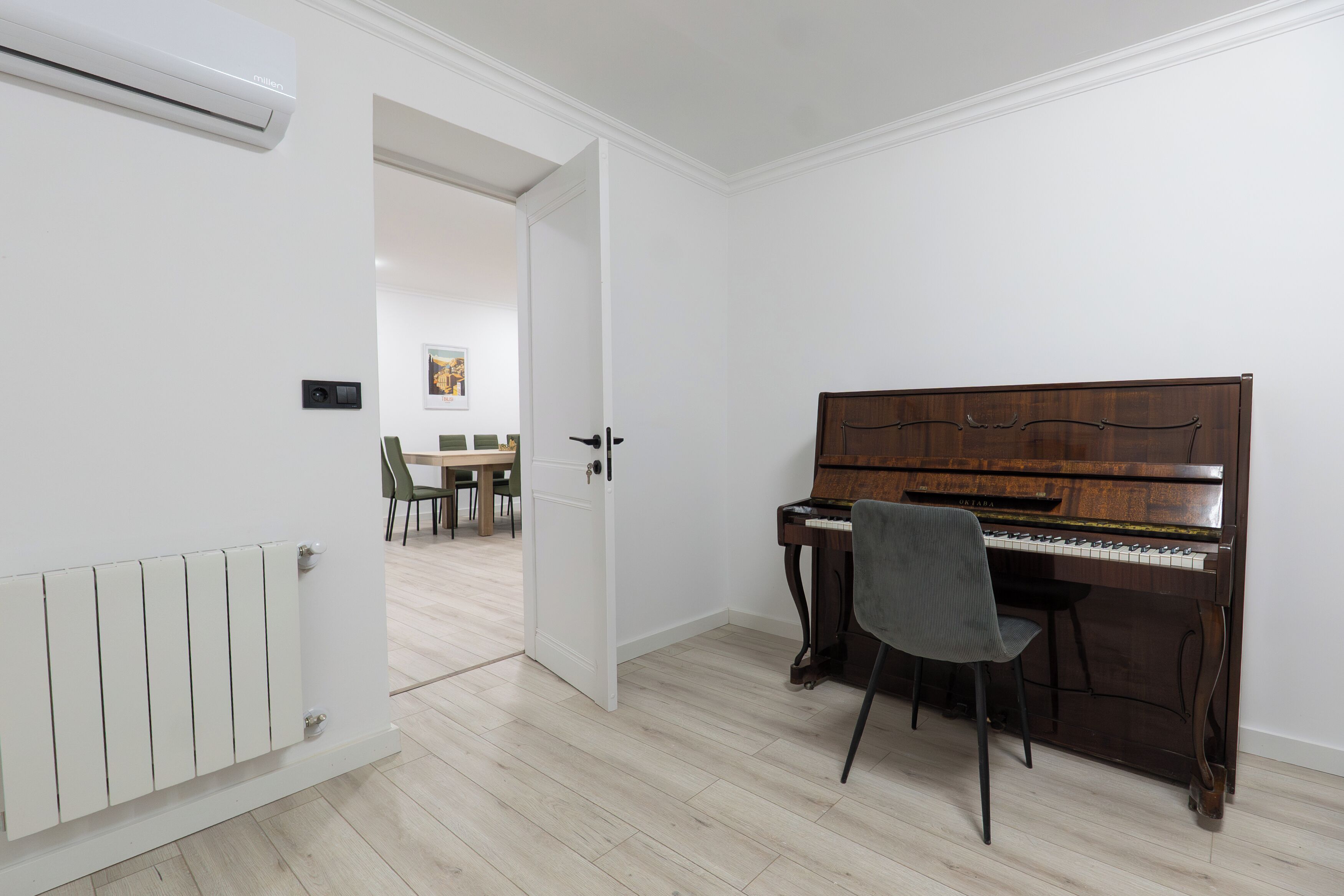 A room with a piano, a radiator, and a door leading to another room.