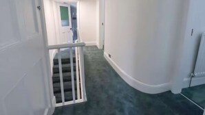 A hallway with a staircase, white walls, and a green carpet. - Stylish Home In Loftus (Loftus)