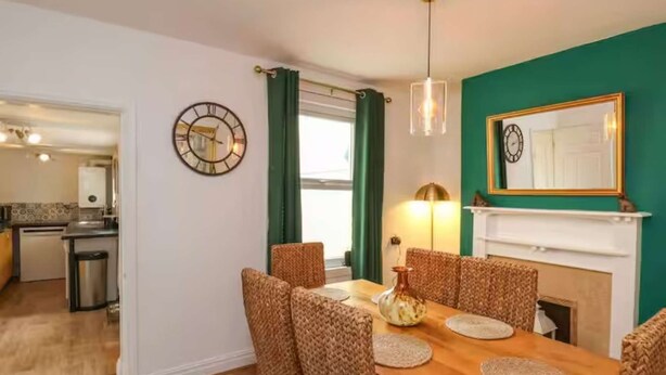 A dining area with a wooden table, woven chairs, a vase, and a mirror above a fireplace. - Stylish Home In Loftus (Loftus)