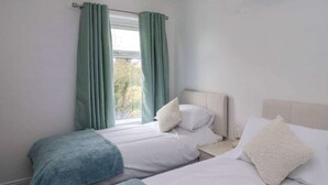 A hotel room with two beds, a window with curtains, a bedside table, and a lamp. - Stylish Home In Loftus (Loftus)