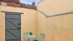 A small outdoor area with a grey door, two turquoise chairs, a small round table, and a yellow patterned rug. - Stylish Home In Loftus (Loftus)