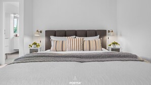 Ein modernes Schlafzimmer mit einem großen Bett, einer dunklen Kopfteil und zwei Nachttischen mit Lampen.