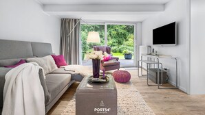 Ein modernes Wohnzimmer mit einem grauen Sofa, einem Couchtisch mit Vase und Kerzen, einem Fernseher und einer Schiebetür zum Garten.