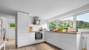 Eine moderne Küche mit weißen Schränken, einem eingebauten Backofen und einem großen Fenster mit Blick auf Grünflächen.