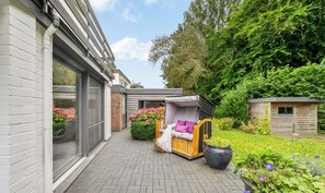 Un espace patio avec un banc en bois, un coin salon abrité et une plante en pot.