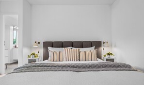Une chambre à coucher moderne avec un grand lit, une tête de lit sombre et deux tables de chevet avec des lampes.