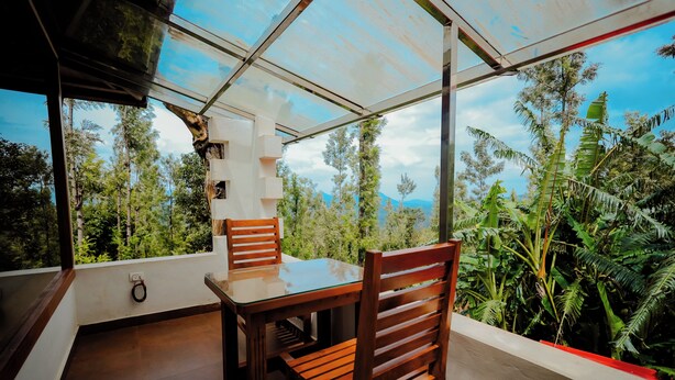 A room with a glass ceiling, wooden furniture, and a view of a forest and mountains. - Anvitha Mansions (Chikkamagaluru)